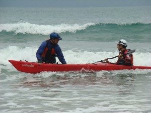 Sea kayaker learning to surf with the help of an instructor.
