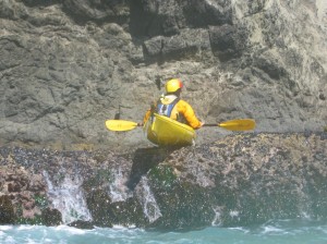 Sea kayaker resting on top of rocks waiting for the next surge.